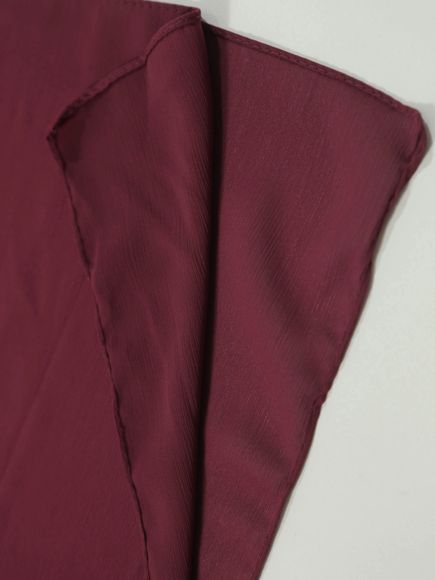 Close-up of soft textured fabric in deep maroon shade, Crinkle Georgette - Maroon material folded neatly.