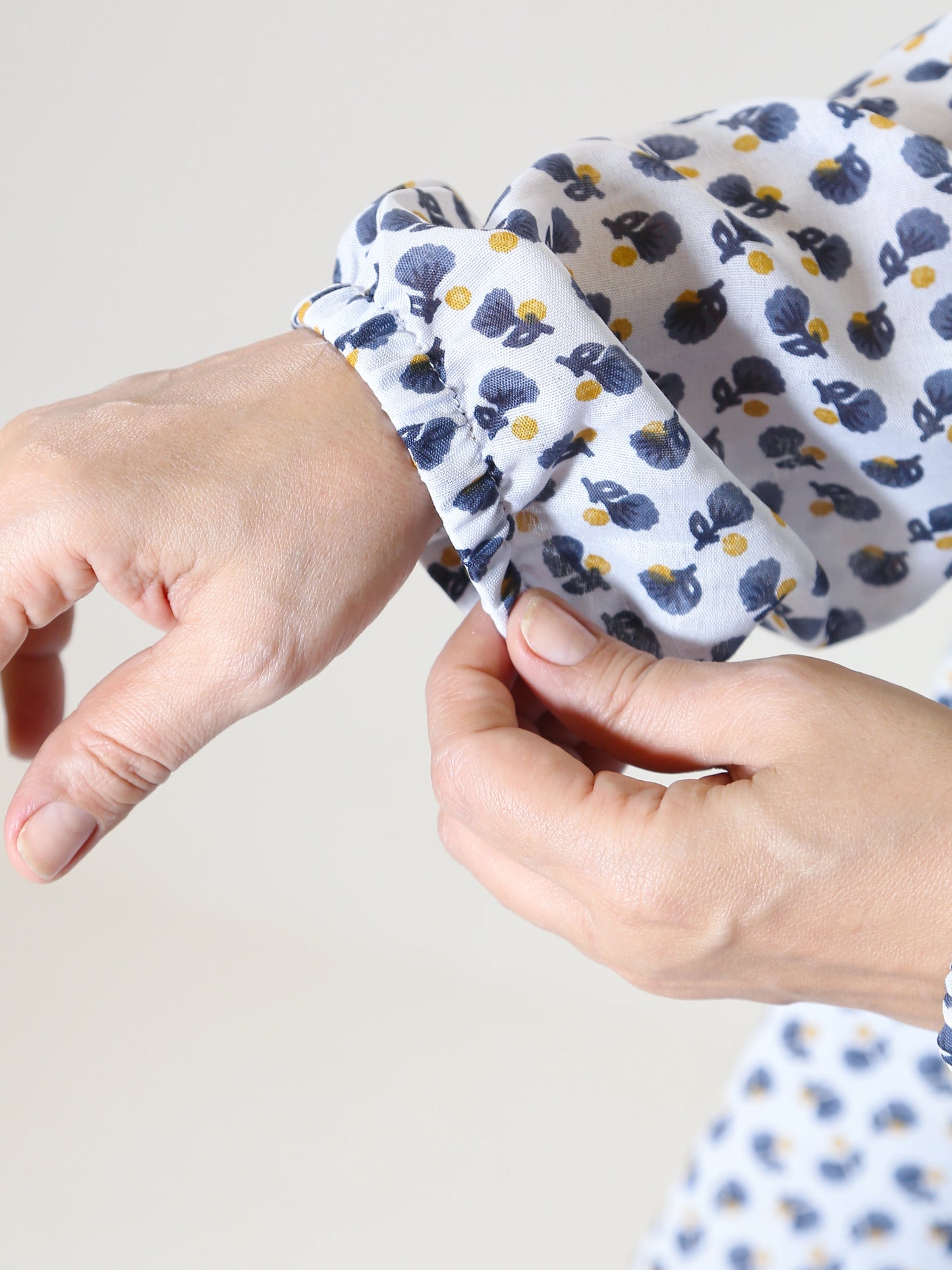 Close-up of a child's hand wearing a patterned shirt with another hand adjusting the sleeve.