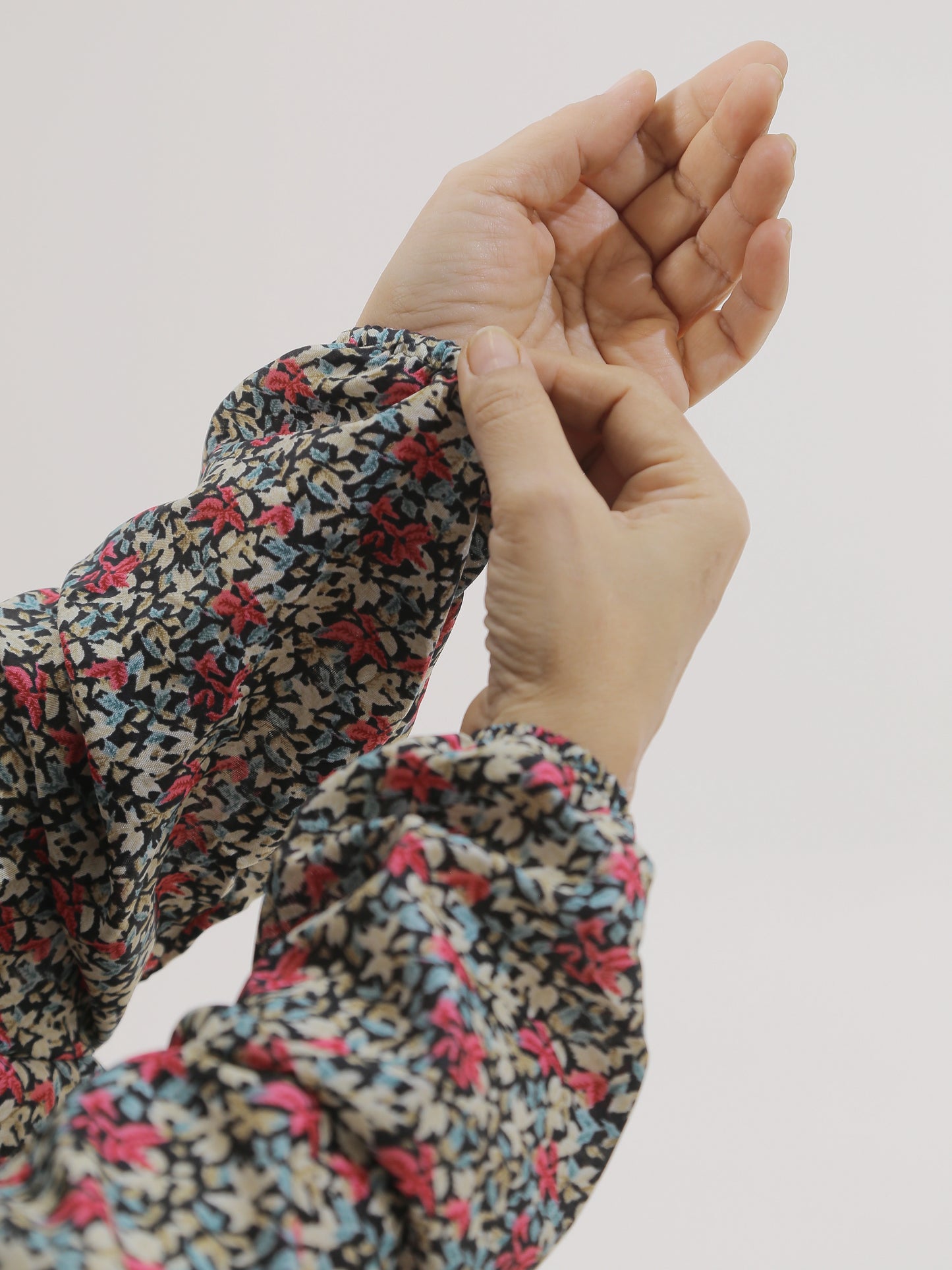 Close-up of hands wearing a floral-patterned garment against a plain background