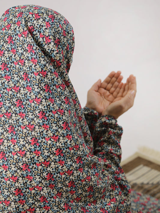 Person wearing a floral headscarf with hands raised, blurred background