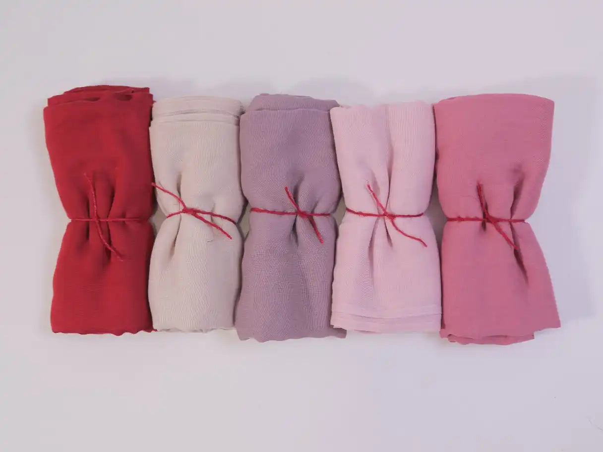 Five folded fabrics in red, beige, purple, pink, and rose on a white background