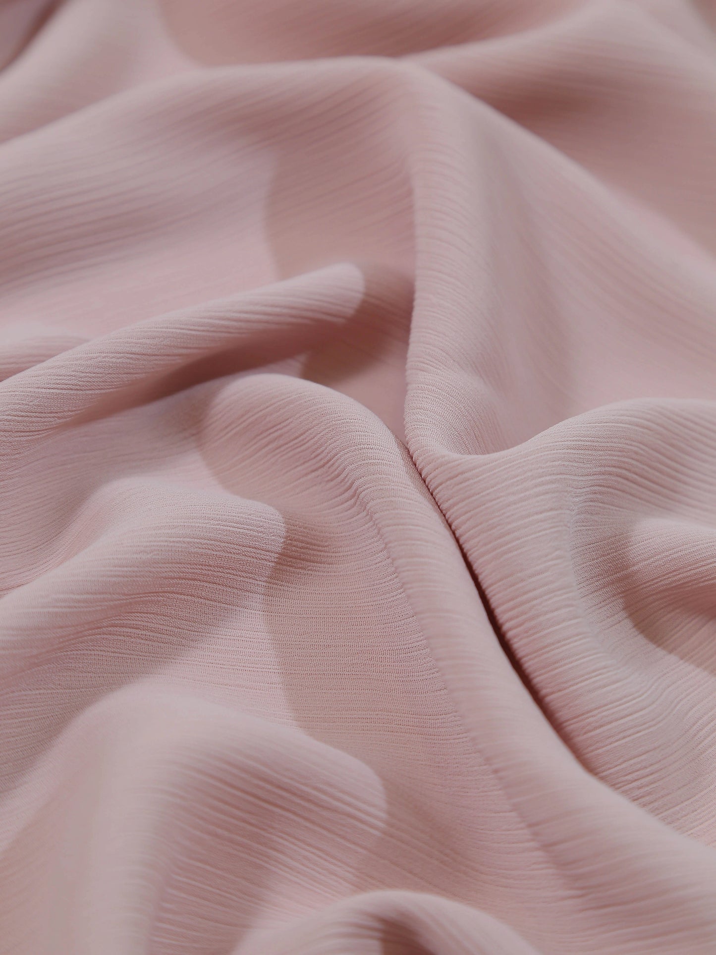 Close-up of soft textured fabric in light pink shade named Crinkle Georgette - Powder Pink with delicate folds and waves.
