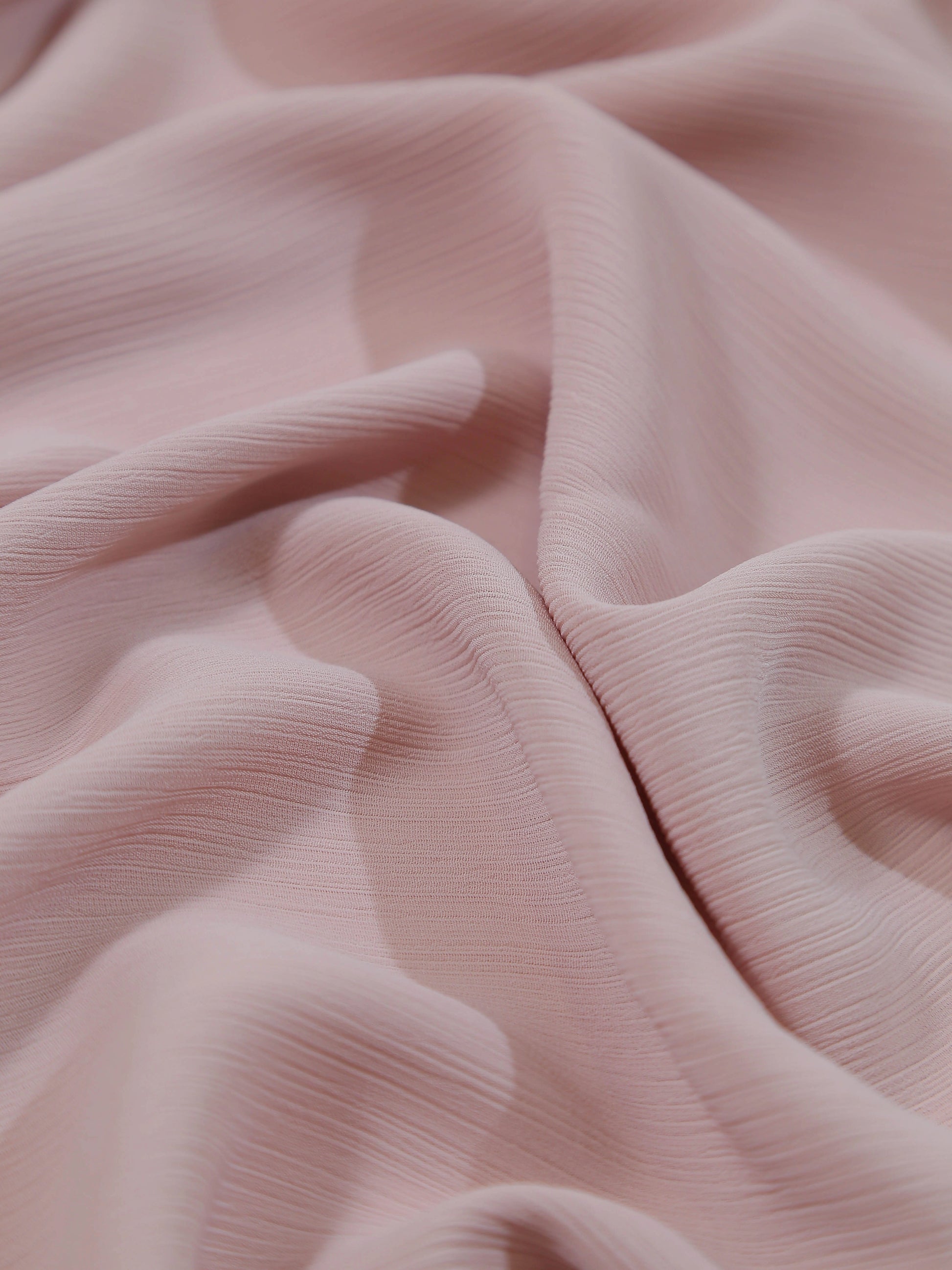 Close-up of soft textured fabric in light pink shade named Crinkle Georgette - Powder Pink with delicate folds and waves.