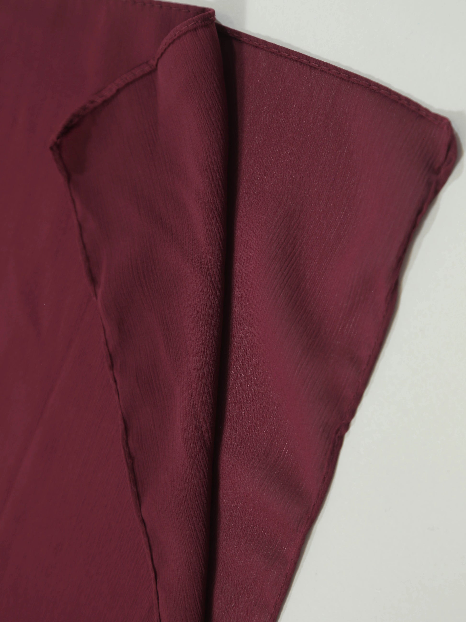 Close-up of soft textured fabric in deep maroon shade, Crinkle Georgette - Maroon material folded neatly.