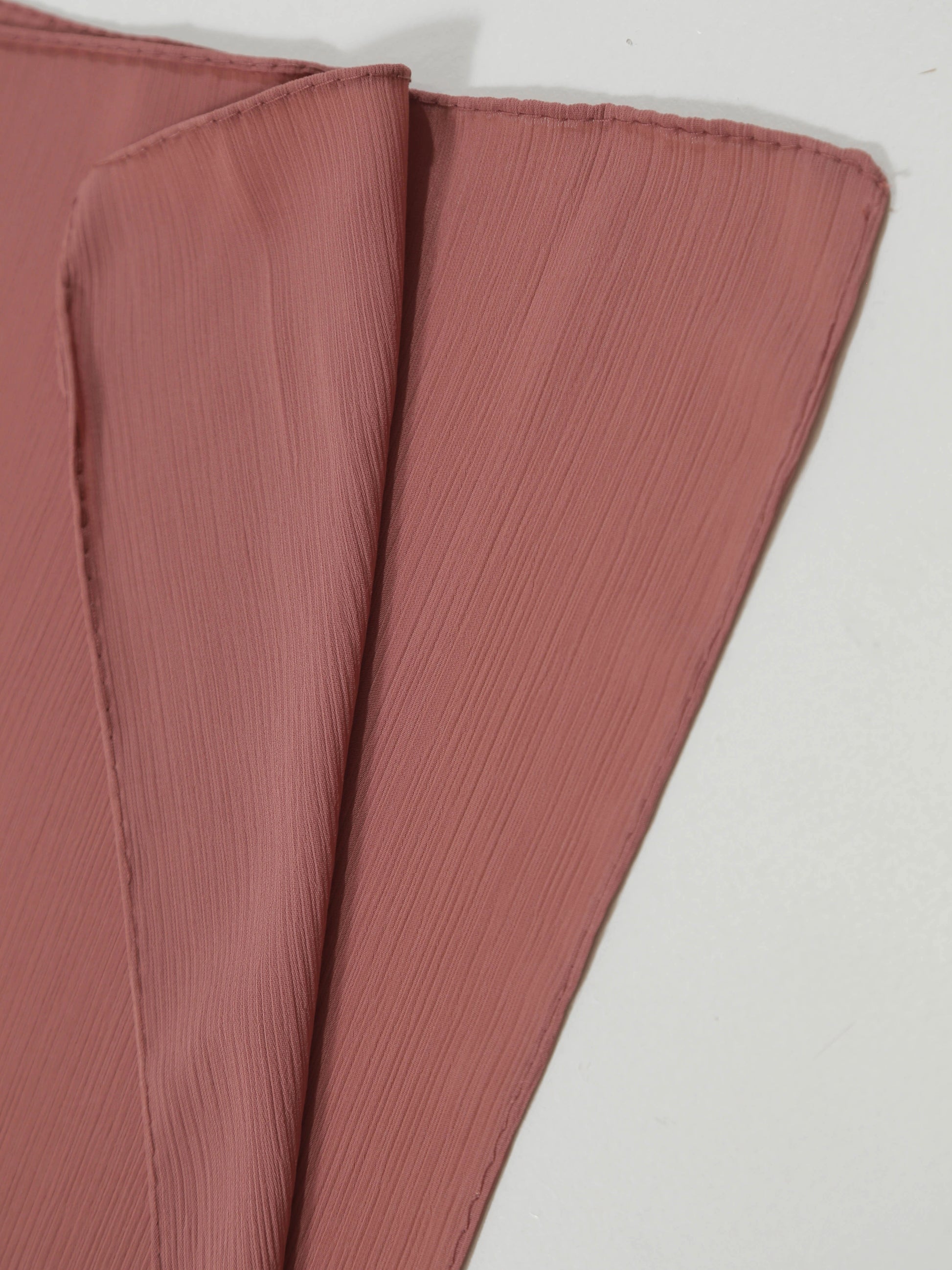 Close-up of soft textured fabric in muted pink shade folded to show crinkle surface, Crinkle Georgette - Pink.