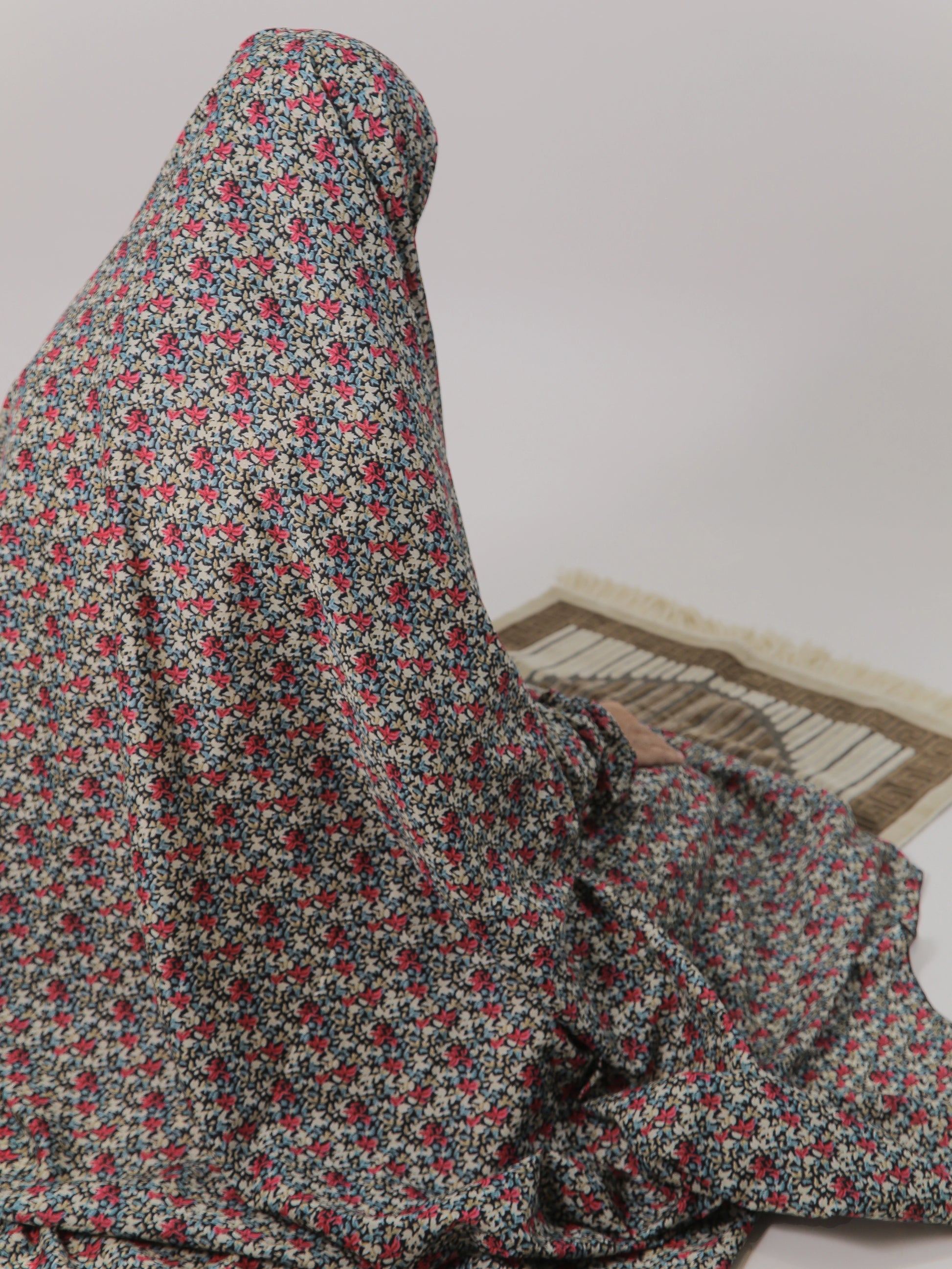 Person wearing a floral hijab sitting on a mat with a plain background