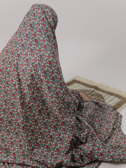 Person wearing a floral hijab sitting on a mat with a plain background