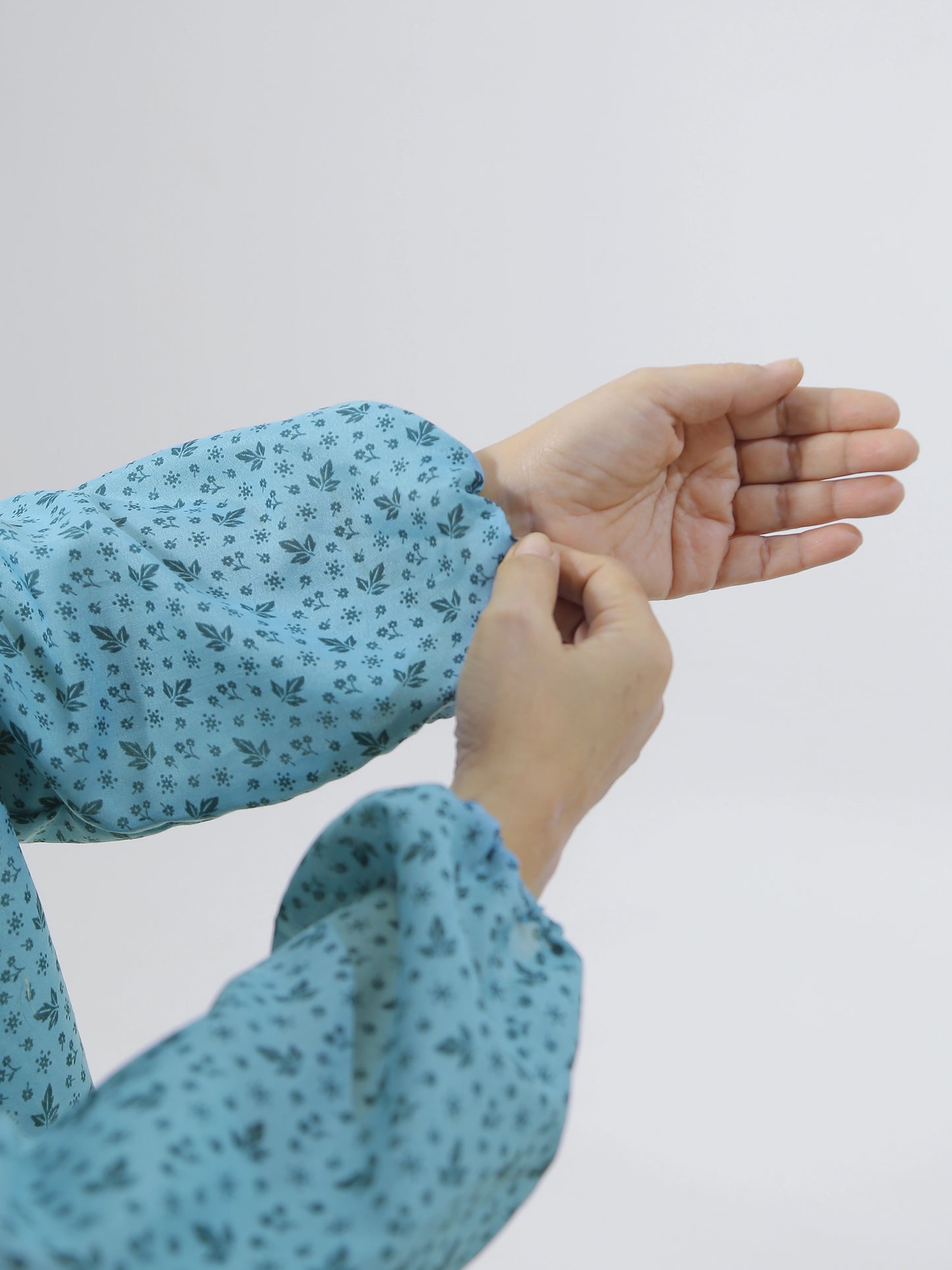 Person wearing a blue floral-patterned long-sleeve shirt against a white background