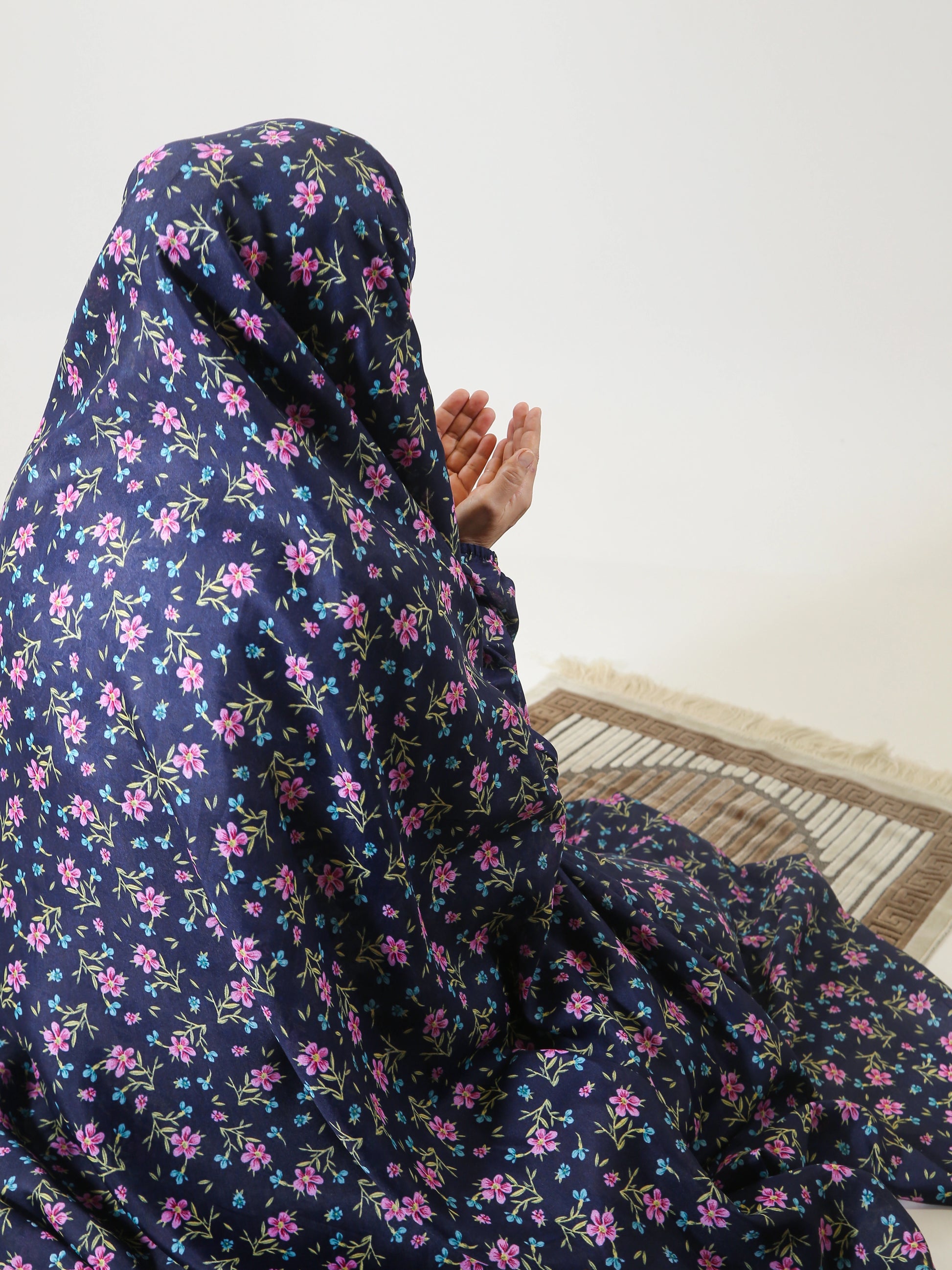 Person wearing a dark blue floral hijab sitting on a wooden floor.