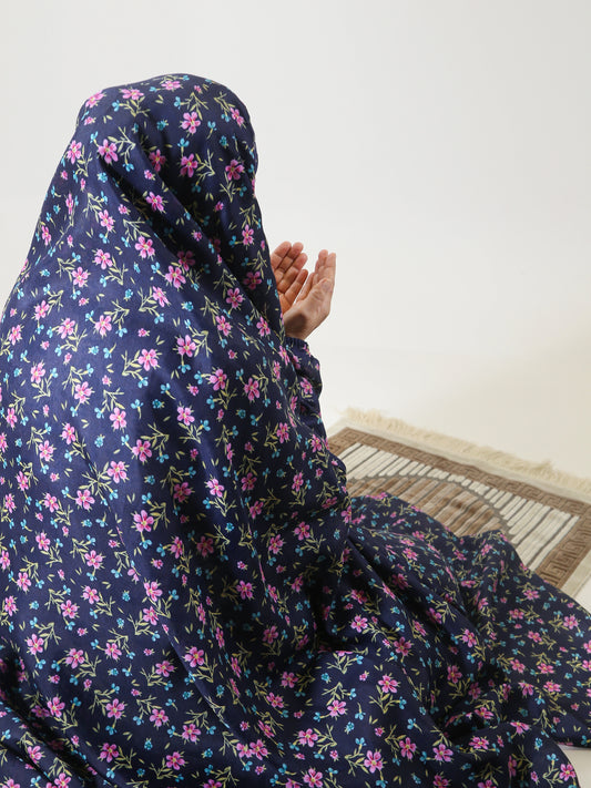 Person wearing a dark blue floral hijab sitting on a wooden floor.