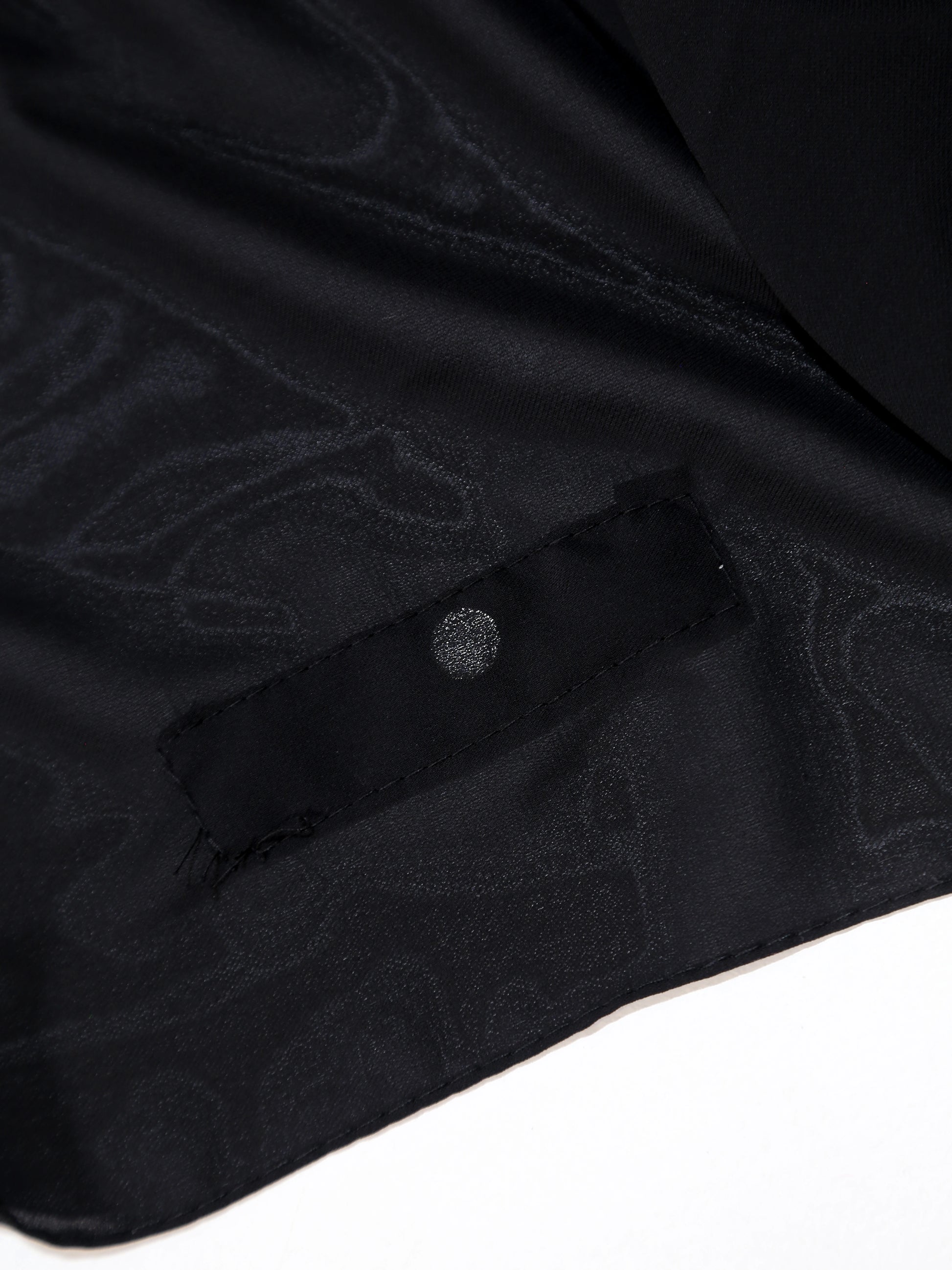 Close-up of a black shirt with a button and subtle pattern on a white background